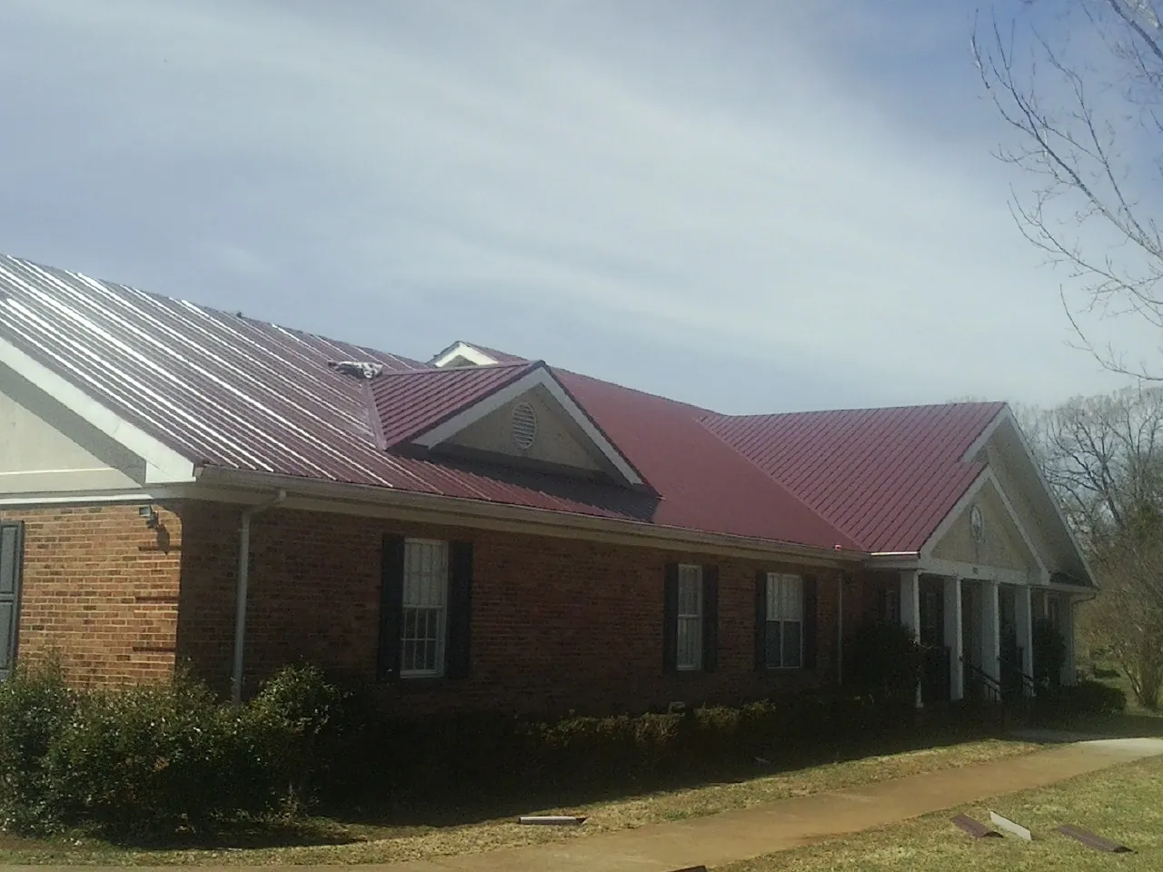 Red metal roof with gabled entries on a long brick building, from a Hail Damage Roof Repair job in East Troy