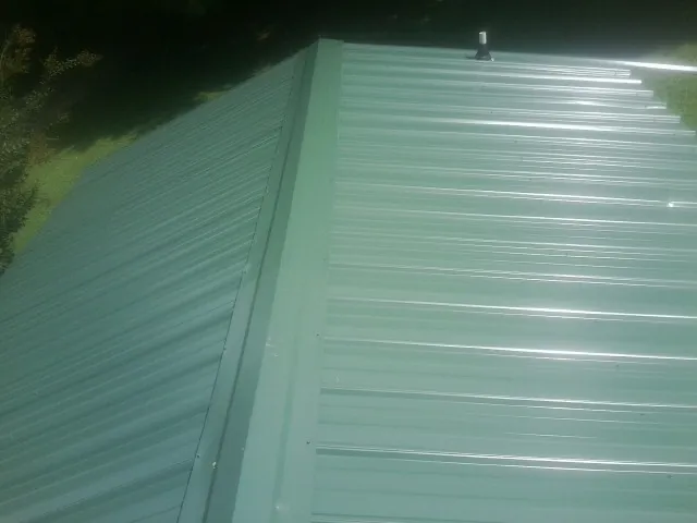 New green metal panels meeting at the ridge of a roof — Flat Roof Repair work by our crew in East Troy
