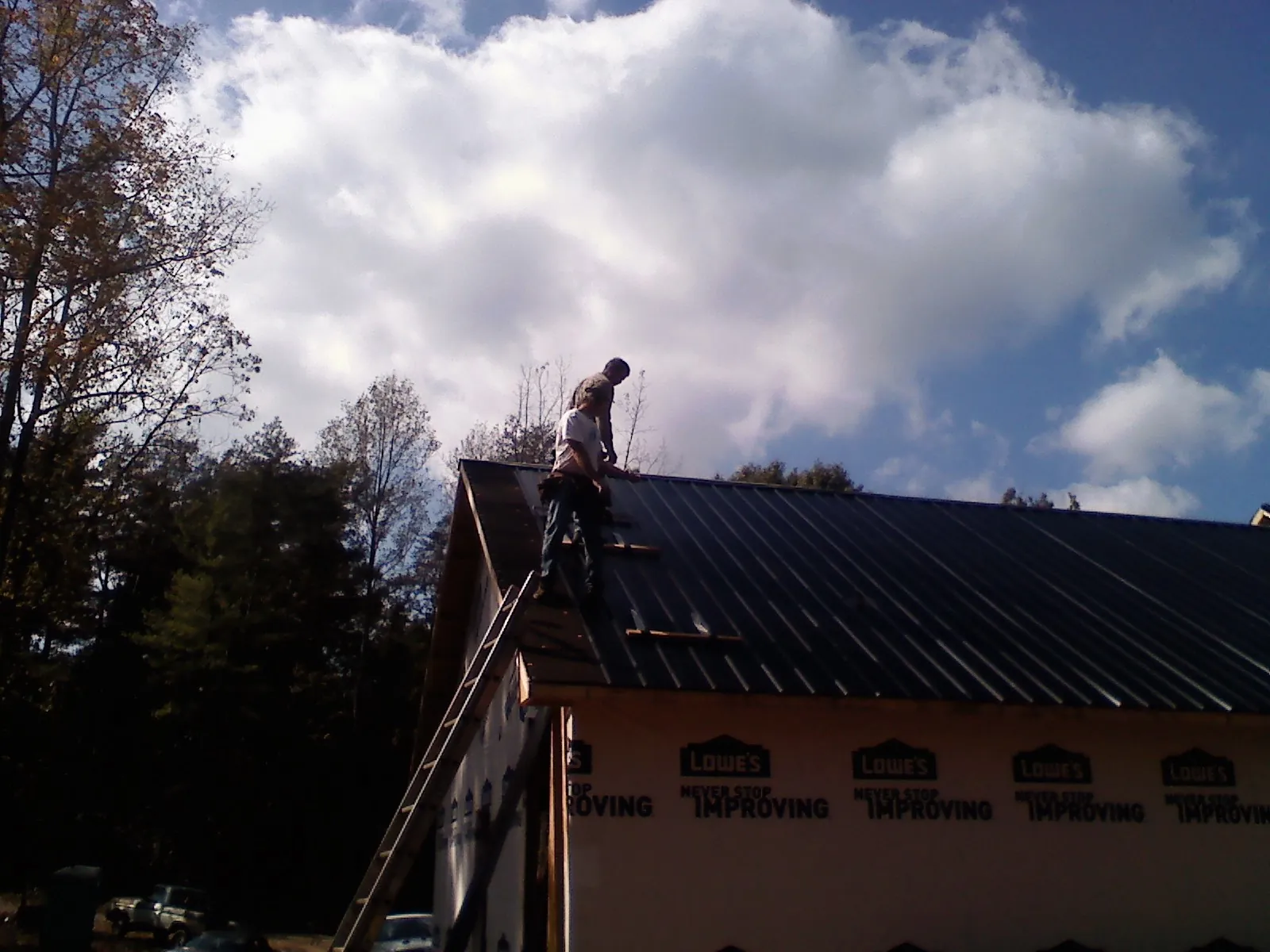 Roofer fastening dark metal panels high against a cloudy sky, from a Roof Inspection job in East Troy