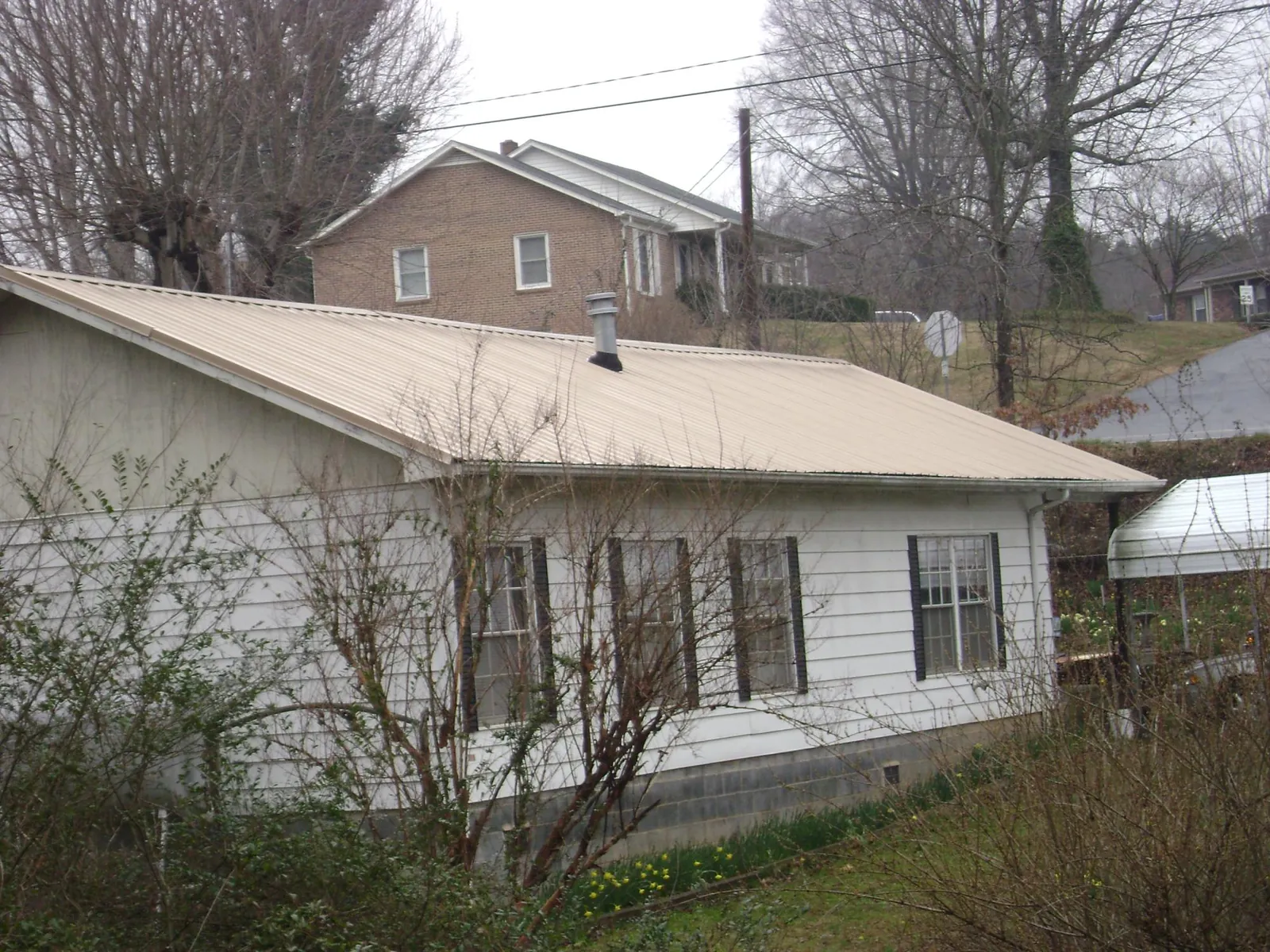 Tan metal roof on a white sided house set into a hillside — Commercial Roofing by Roofing Brothers in East Troy