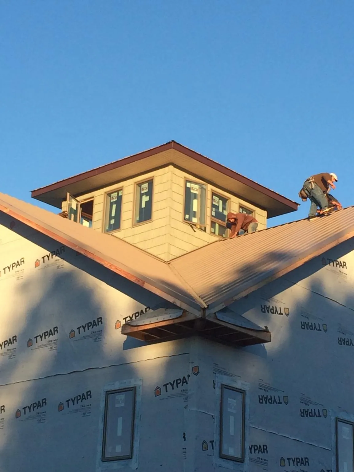 Roofers working around a rooftop cupola on a new metal roof at sunset — Roof Waterproofing in East Troy by Roofing Brothers